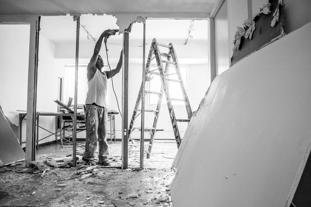 Werkman op een ladder aan het plafond, met gipsplaten tegen de muur